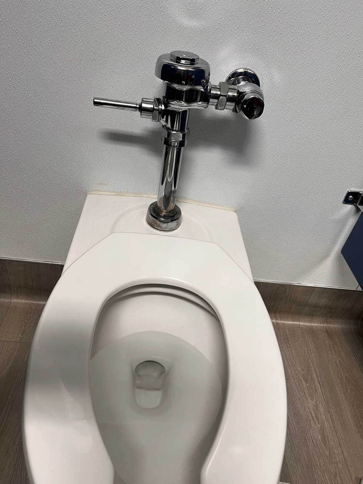 Commercial toilet with a wall-mounted chrome flush valve.