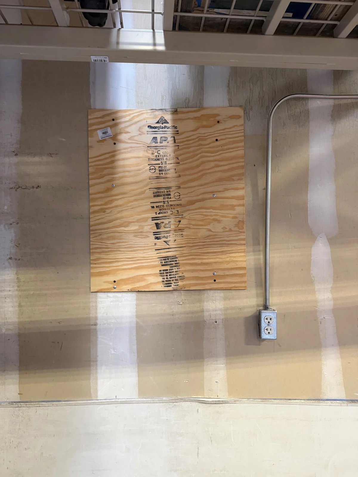 A plywood panel screwed over a wall area behind storage shelving.